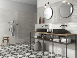 Elegancka łazienka z podłogą wyłożoną płytkami patchworkowymi Nora Coal ze stołem z dwiema czarnymi umywalkami nablatowymi i dwoma okrągłymi lustrami z kinkietami
