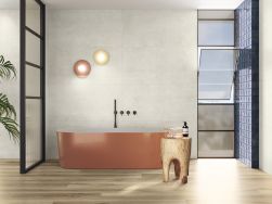 Łazienka ze ścianami wyłożonymi beżowymi płytkami imitującymi beton Raw Naive Smooth z błyszczącą wanną w kolorze łososiowym, taboretem i dwoma kulistymi kinkietami
