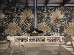 Pomieszczenie ze ścianą wyłożoną dekoracyjnymi płytkami w brązowe liście z kolekcji Atelier z kominkiem, szafką na drewno, dywanem i dwoma krzesłami