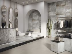 Ekskluzywny sklep wyłożony szarymi płytkami imitującymi metal Reef White z białą kanapą i pufami, lustrami, odzieżą, akcesoriami i ladą