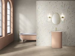 Łazienka ze ścianą wyłożoną beżowymi płytkami imitującymi beton Raw Naive z różową wanną i umywalką stojącą oraz lustrem w złotej ramie