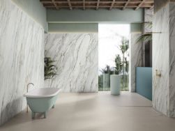 Łazienka z podłogą wyłożoną beżowymi płytkami imitującymi beton Raw Cotton, z marmurowymi ścianami, z wanną wolnostojącą i stojącą umywalką w miętowym kolorze oraz z prysznicem