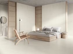 Sypialnia wyłożona beżowymi płytkami imitującymi beton Raw Naive Smoth z podwójnym łóżkiem, krzesłem, lampą stojącą i małym stolikiem