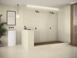 Łazienka wyłożona beżowymi płytkami imitującymi beton Raw Cotton z białą umywalką stojącą, lustrem w czarnej ramie, lampą wisząca i dwoma prysznicami