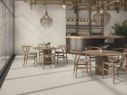 Restauracja wyłożona białymi płytkami lastryko Abyss White z barem, okrągłymi stolikami, krzesłami i lampami wiszącymi