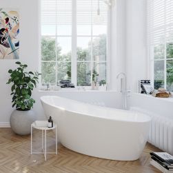 Pokój kąpielowy z drewnianą podłogą, białą wanną wolnostojącą Bellis pod oknami, baterią wolnostojącą, kwiatem w donicy, obrazem na ścianie, kosmetykami i książkami