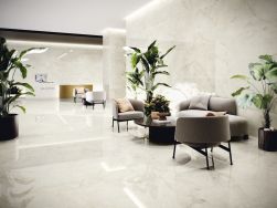 Nowoczesne lobby recepcyjne wyłożone błyszczącymi płytkami imitującymi marmur, z szarymi meblami wypoczynkowymi, czarnym stolikiem kawowym i dużymi roślinami doniczkowymi.