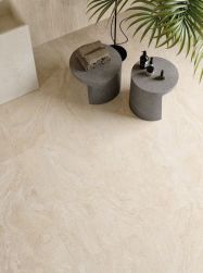 Beżowa podłoga Provenza Unique Travertine Cream, dwa szare betonowe stoliki z ręcznikami i kosmetykami oraz liście palmy w nowoczesnym wnętrzu.