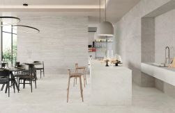 Elegancka restauracja: jasne płytki Provenza Unique Travertine, biała wyspa z hokerami, czarne stoły, nowoczesne okrągłe lampy i duże przeszklenia.