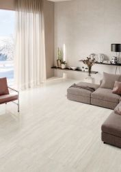 Salon z podłogą Provenza Unique Travertine White Vein, beżową sofą modułową i szarymi zasłonami. Jasne wnętrze z widokiem na zimowy krajobraz za oknem.