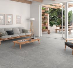 Wizualizacja nowoczesnego salonu otwartego na taras. Wnętrze wykończone szarymi płytkami Lithos Grey o strukturze kamienia, wyposażone w jasną sofę, drewniany stolik i minimalistyczne meble.