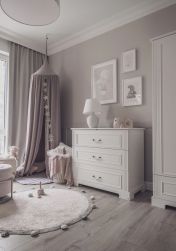 Przytulny pok&oacute;j dziecięcy w szaro-białej tonacji. Wnętrze zdobi klasyczna komoda, wiszący baldachim z kącikiem do zabawy, okrągły dywan z pomponami oraz urocze obrazki w ramkach na ścianie.