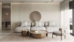 Jasny salon w stylu minimalistycznym. Beżowa kanapa i fotel stoją na dywanie. Na ścianie wiszą pionowe lamele oraz duża, okrągła, podświetlana płaskorzeźba. Z przodu niskie stoliki kawowe.