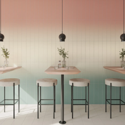 Nowoczesna kawiarnia stoliki, hokery oraz wiszace nad stolikami lampy na tle gradient&oacute;w płytek