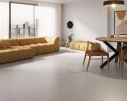 Nowoczesny salon z dużą ż&oacute;łtą sofą i częścią jadalną z drewnianym stołem na tle okna z widokiem na miasto, wyłożony płytkami podłogowymi Pamesa Lin.