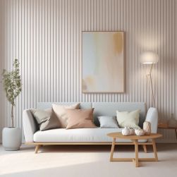 Jasny salon w stylu boho. Biała kanapa z poduszkami stoi na tle ściany z pionowych lameli. Nad nią wisi abstrakcyjny obraz w drewnianej ramie, z boku lampa stojąca, stolik i roślina w donicy.