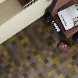 Wizualizacja podłogi z lotu ptaka z drobną mozaiką w odcieniach oliwki, brązu, ochry i fioletu. W prawym g&oacute;rnym rogu widać brązowy fotel z otwartą książką &bdquo;Belgian Modern&rdquo;, leżący obok bordowy notes oraz fragment beżowych płytek ściennych.