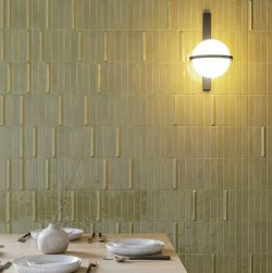 Zielone pieknie odbijające światło cegiełki w resutaracji z lampą kinkietową