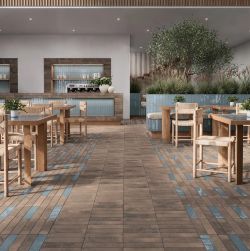 Wnętrze restauracji lub kawiarni z podłogą wyłożoną brązowymi i niebieskimi płytkami drewnianymi stołami i krzesłami barem z niebieskimi kaflami i dużą rośliną doniczkową w głębi.