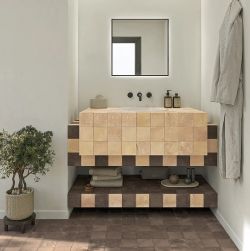 Nowoczesna łazienka z podwieszanymi meblami wyłożonymi beżowymi i ciemnobrązowymi kwadratowymi płytkami czarnym lustrem nad umywalką rośliną doniczkową po lewej i szlafrokiem po prawej stronie.