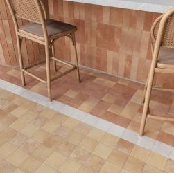 Nowoczesne wnętrze baru z podłogą i ścianą wyłożoną terakotowymi i beżowymi płytkami, oraz dwoma wiklinowymi hokerami.