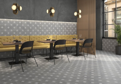 Wnętrze restauracji, trzy stoliki, pod ścianą żółte tapicerowane siedziska, przy stolikach czarne krzesła, na ścianie i podłodze płytki Ponent Grey 22,3x22,3 płytki patchworkowe