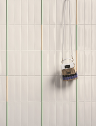 Ściana wyłożona białymi płytkami z kolekcji Kappa, na ścianie zawieszona torebka, między płytkami Kappa Matita Aloe 1,1x20 listwa dekoracyjna