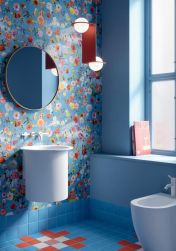 Łazienka, na ścianie podwieszana biała umywalka, pod oknem bidet, nad umywalką okrągłe lustro, na podłodze płytki w kolorze niebieskim i czerwonym, na ścianie płytki PAPER41 PRO – MIA 50x100