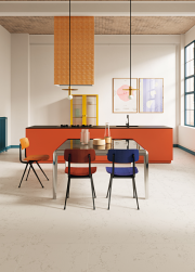 Kuchnia, duża wyspa w kolorze pomarańczowym, obok stół ze szklanym blatem, przy stole kolorowe krzesła, na podłodze płytki Superclassica SCW Natural 30x60 płytki imitujące kamień
