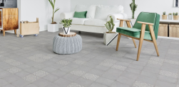 Salon, pod ścianą kanapa w białym kolorze, zielone krzesło, na środku dekoracyjny mały stolik, rośliny w doniczkach, na podłodze szare płytki bazowe i Triana Flor Gris 25x25 płytka dekoracyjna patchworkowa