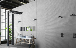 Pod ścianą na blacie dwie umywalki, małe prostokątne lustro, obok prysznic, ściana pod prysznicem wyłożona dekoracyjnymi płytkami, ściana przy umywalce wyłożona Trend Gris 40x120 płytka imitująca beton