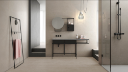 Łazienka wyłożona beżowymi płytkami imitującymi beton z kolekcji Start z kabiną prysznicową, szafką z umywalką, okrągłym lustrem i drabiną z ręcznikiem