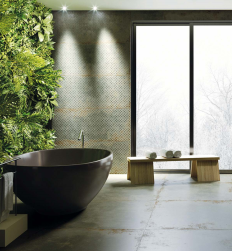 Czarna wanna wolnostojąca, przy dużym oknie drewniana ławka z ręcznikami kąpielowymi, na ścianie dekoracyjne zielone płytki, na podłodze Flamed Green Natural Rect. 59,55x59,55 płytki imitujące metal