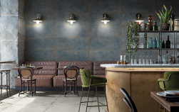 Restauracja, brązowe stoliki i krzesła, przy ścianie brązowa kanapa, dekoracyjne czarne lampy, podłoga wyłożona białymi płytkami imitującymi metal, na ścianie Flamed Sapphire Matte Rect. 44,63x119,3 płytki ścienne imitujące metal