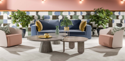 W salonie kanapa w niebieskim odcieniu, dwa beżowe fotele, stolik kawowy, na podłodze białe płytki imitujące beton, ściana wyłożona Mud Stamp Pre 20 Natural 59,2X59,2 płytka dekoracyjna