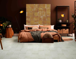 Sypialnia, duże łóżko, narzuta w brązowym kolorze, nad łóżkiem wyłożone dekoracyjne płytki, ściana i meble w brązowym kolorze, podłoga wyłożona Mud White Natural 24,9x100 płytka imitująca beton