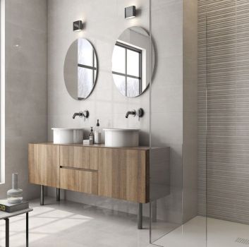 Beżowa łazienka z prysznicem, drewnianą półką na której stoją dwie umywalki nablatowe oraz okrągłymi lustrami