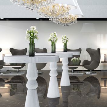 Biały salon z okazałymi żyrandolami, białymi stolikami z marmuru oraz geometrycznymi stolikami z kubełkowymi fotelami