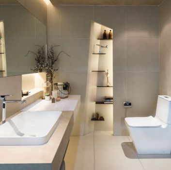 Szara łazienka z toaletą, podświetloną wnęką na dekorację oraz jasnym blatem z wbudowaną umywalką i lustrem