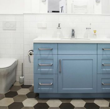 Biało-szara łazienka z zabudowaną wanną, niebieską szafką z wbudowaną umywalką oraz toaletą