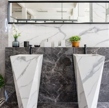 Łazienka wyłożona płytkami imitującymi marmur z dwiema stojącymi umywalkami i długim lustrem