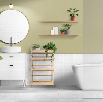 Biało-zielona łazienka z wanną, białą szafką z umywalką nablatową, półkami z kwiatami i okrągłym lustrem