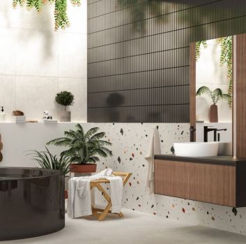 Oryginalna łazienka z jedną częścią ściany wyłożoną kolorowymi płytkami lastryko, z ciemną okrągłą wanną, wiszącą szafką drewnianą z umywalką nablatową i lustrem, kwiatami i kosmetykami