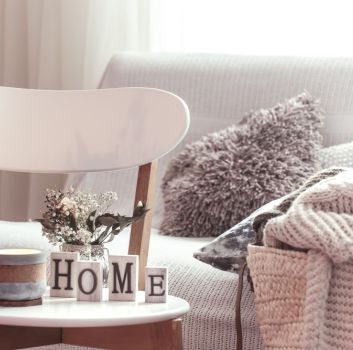 Przytulny pokój z jasną kanapą z poduszkami i kocami i krzesłem z napisem home