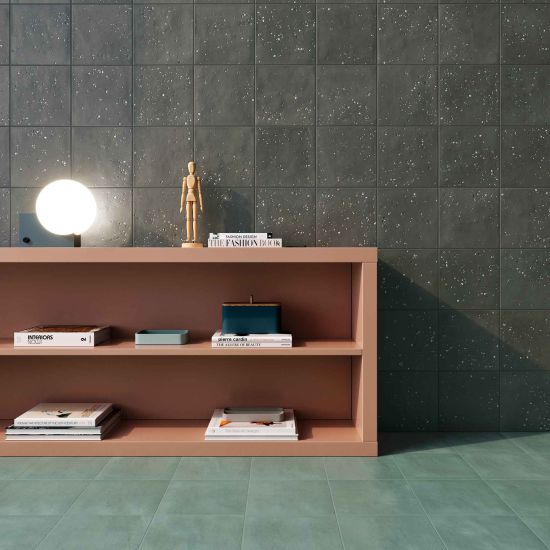 Pok&oacute;j ze ścianą wyłożoną ciemnymi płytkami dekoracyjnymi Stardust Pebbles Nero, z zieloną podłogą i kolorową szafką z książkami i lampką