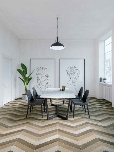 Jadalnia wyłożona drewnopodobnymi płytkami w jodełkę Chevron B Wood Mid na podłodze, z marmurowym stołem, czarnymi krzesłami, dwoma dużymi obrazami, kwiatem w donicy i lampą wiszącą