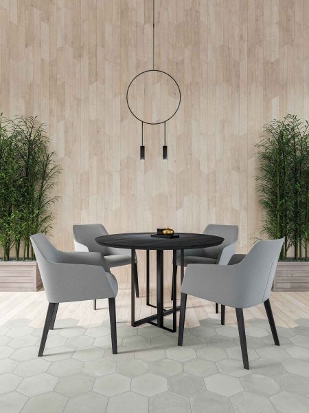 Pok&oacute;j z drewnopodobnymi płytkami w jodełkę Chevron A Wood Light na ścianie i z szarą podłogą, z czarnym okrągłym stolikiem i szarymi krzesłami oraz lampą wiszącą