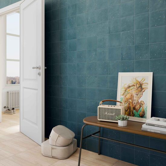 Pok&oacute;j ze ścianą wyłożoną niebieskimi płytkami dekoracyjnymi Stardust Pebbles Ocean, z białymi drzwiami i niskim stolikiem z radiem, obrazem i książkami