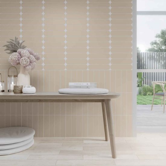 Ściana wyłożona beżowymi cegiełkami Grace O Sand Matt, drewniany st&oacute;ł z kwiatami i świecami oraz białe poduszki