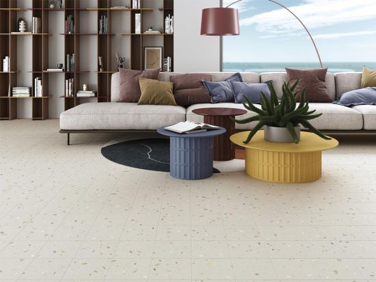 Salon z podłogą wyłożoną jasnymi płytkami lastryko Croccante Tutti Frutti z długą kanapą, trzema okrągłymi stolikami i regałem z książkami